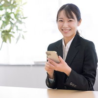 スマホを持ってスマイルする黒いスーツの女性の写真