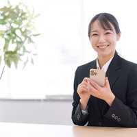 笑顔でスマホを持つスーツ姿の女性の写真