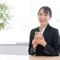 スマートフォン操作を指導する笑顔の女性社員の写真