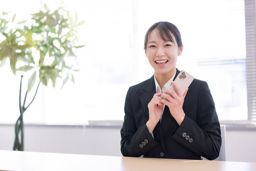 スマホを片手に笑顔の女子社員、受け取ったメッセージに喜ぶ