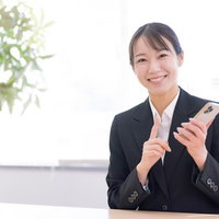 スマートフォンを手に笑顔で接客する女性ショップ店員の写真