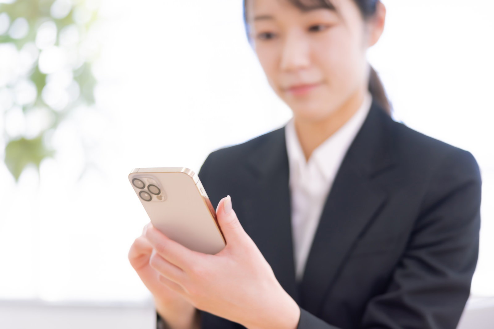 黒いスーツを着た女性がベージュのiPhoneを手に持っている［モデル：SAKI］