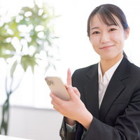 黒いスーツでスマホを操作する笑顔の女性社員の写真