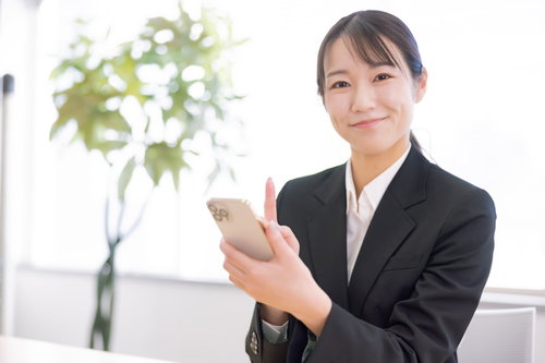 黒いスーツでスマホを操作する笑顔の女性社員