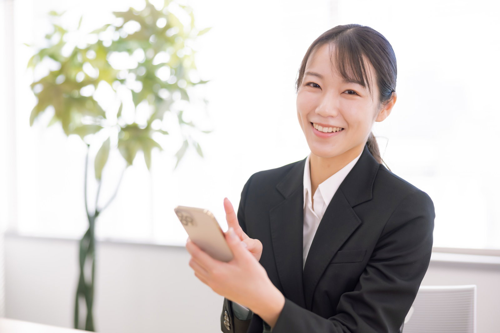 黒いスーツを着てスマホを操作する笑顔の女性［モデル：SAKI］