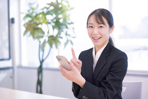 明るいオフィス空間でスマホを操作する笑顔のビジネスウーマン