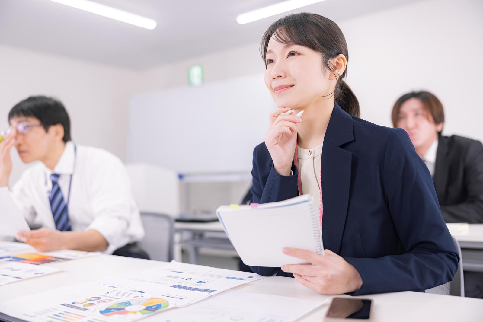 会議室でセミナーに参加し資料を見ている女性と男性の参加者［モデル：SAKI ACE ガーミー］