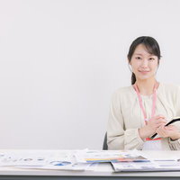 デスク上の資料を整理しながら議事録を取る事務の女性の写真