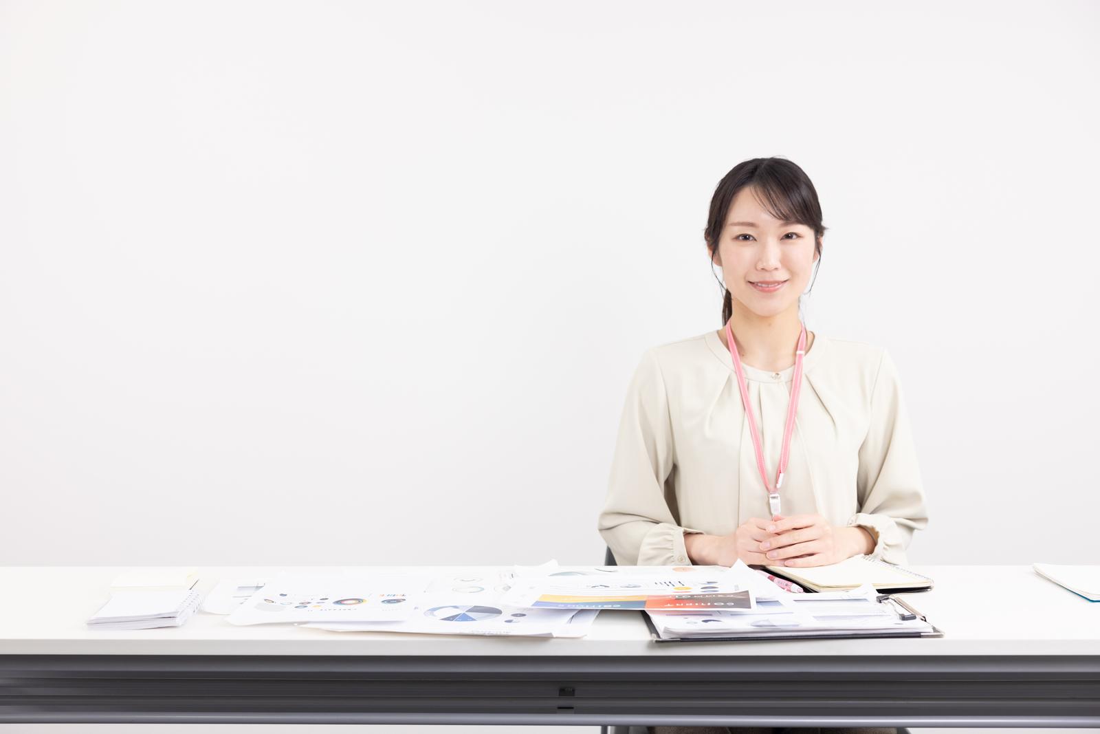 会議室のテーブルで書類を整理するベージュのカーディガンを着た女性［モデル：SAKI］