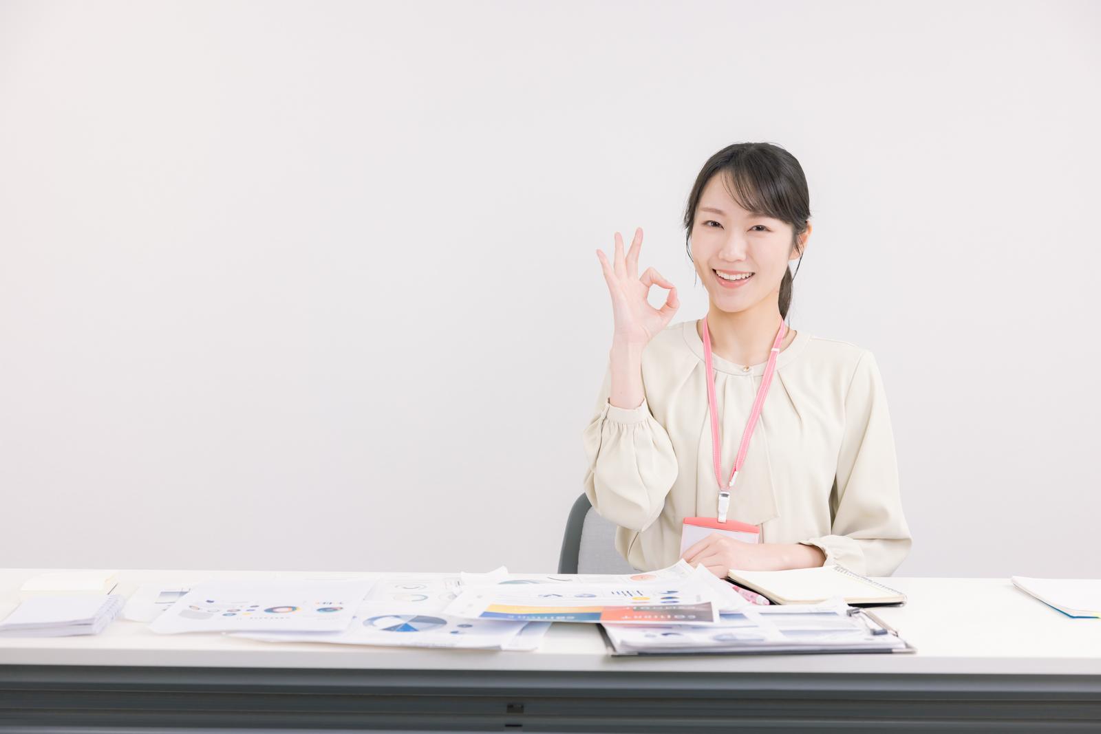 デスクでOKサインをする笑顔の女性社員［モデル：SAKI］
