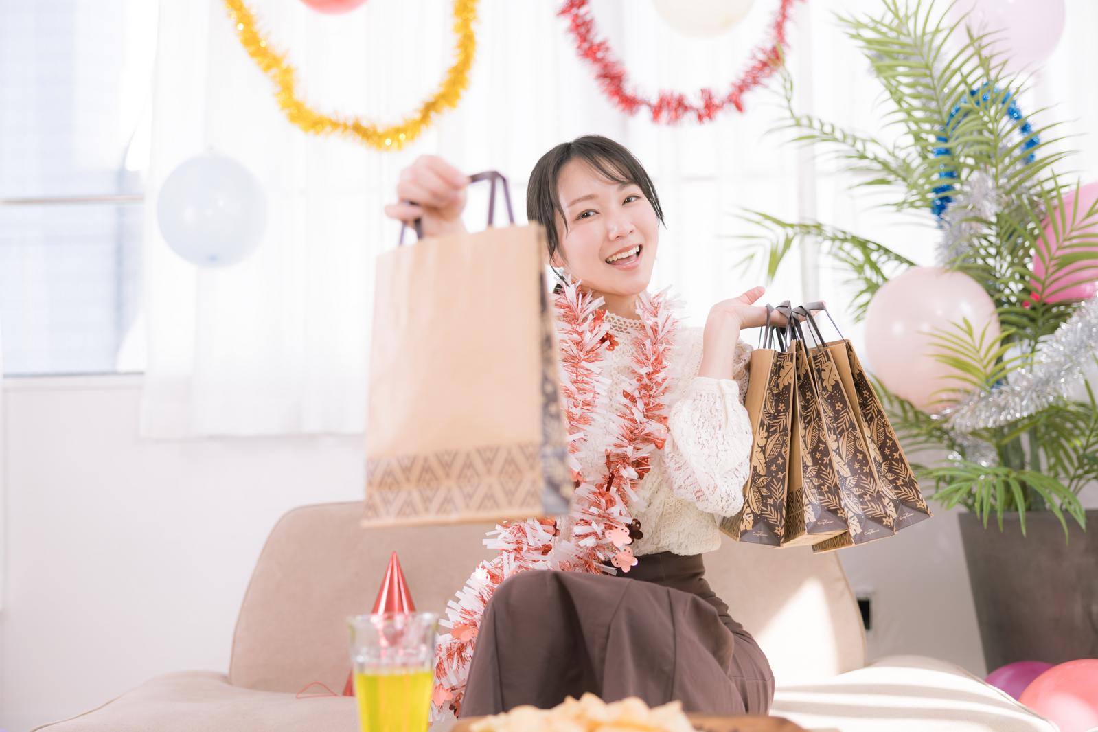 誕生日パーティーでプレゼントを受け取って喜ぶ女性がショッピングバッグを持っている［モデル：SAKI］