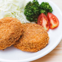 白い皿に盛り付けた揚げたてのコロッケと野菜の付け合わせの写真