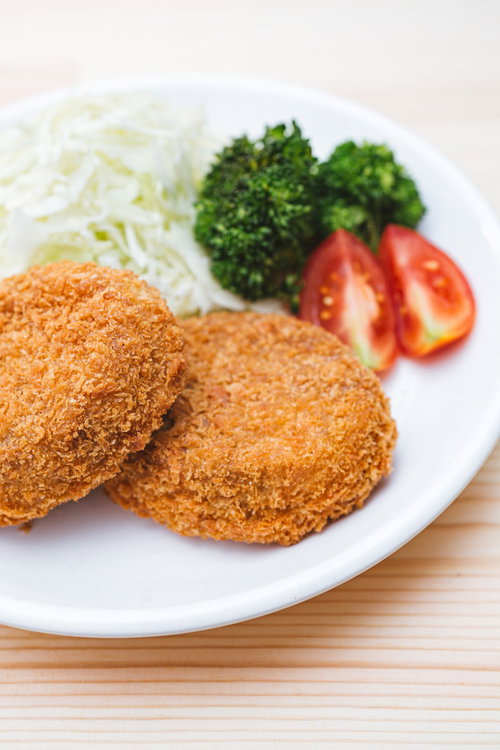 白い皿に盛り付けた揚げたてのコロッケと野菜の付け合わせ