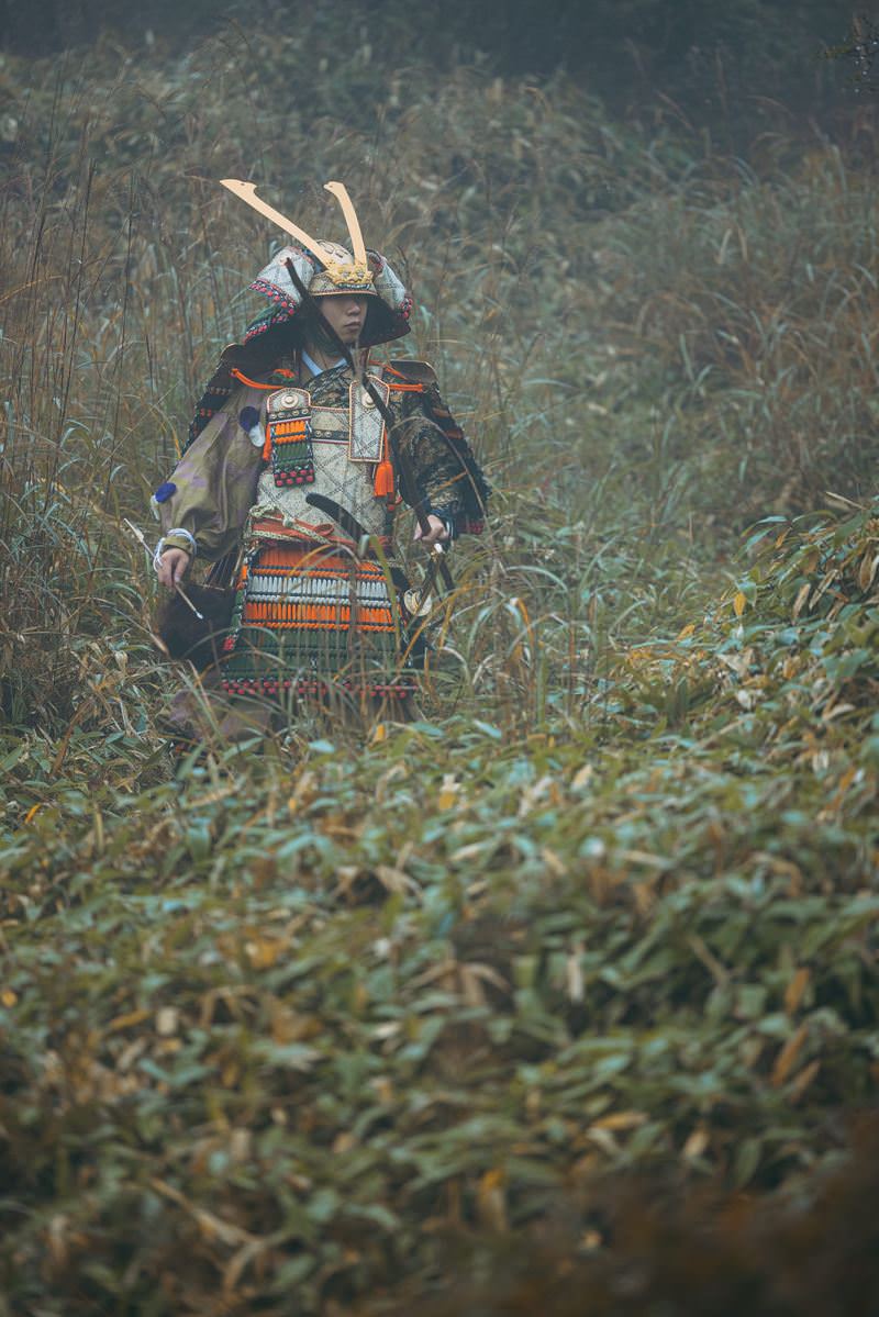 大鎧を着用し弓を持った武士が草原に座る姿［モデル：まーこ］