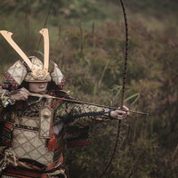 大鎧を身に着けた侍が大弓で狙いを定める姿の写真