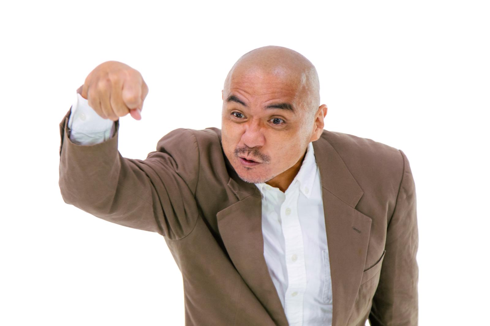 激怒して指を突き立てるスーツ姿の坊主頭の男性［モデル：よたか］