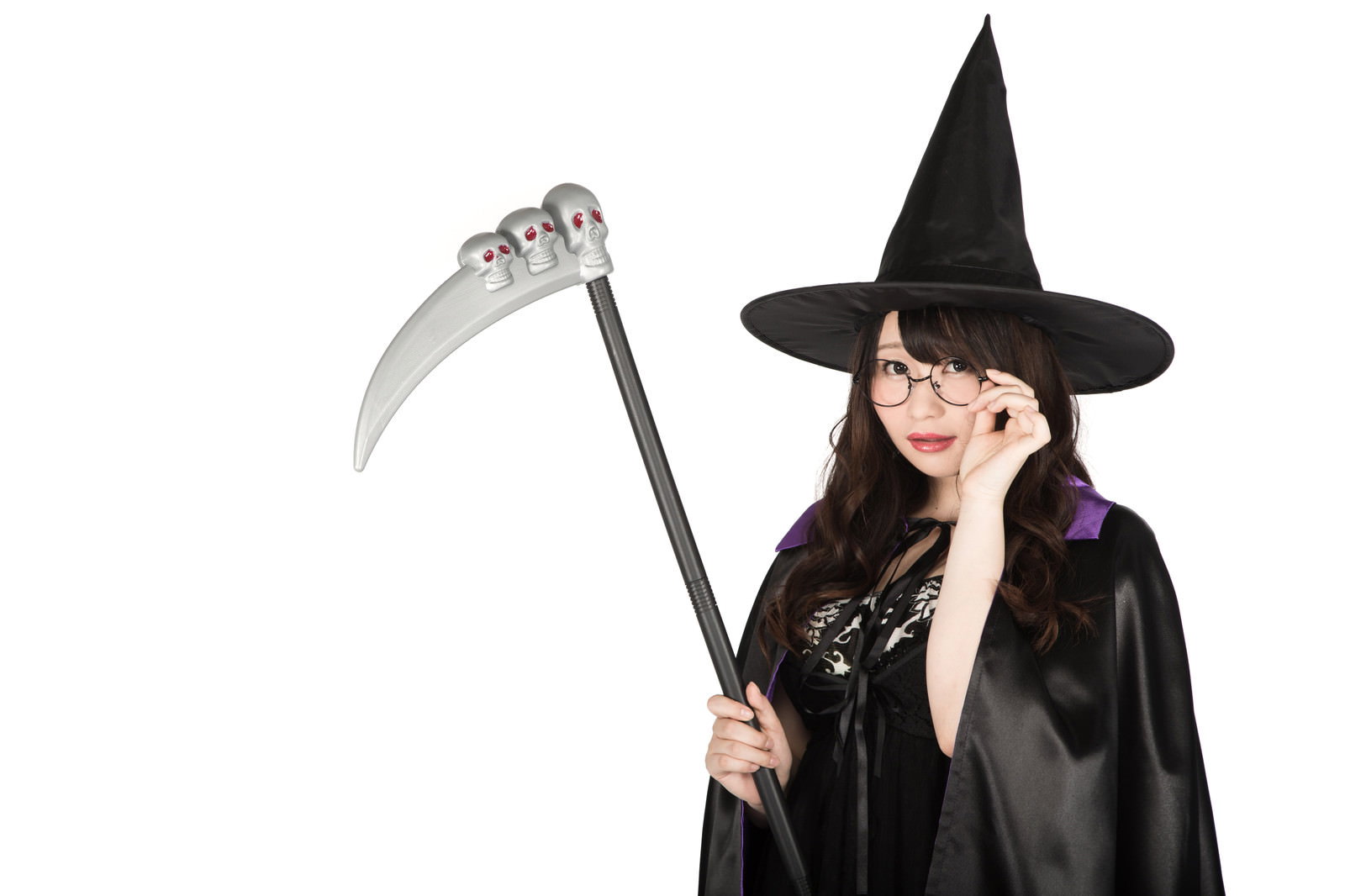 眼鏡をかけた魔女の仮装の女性が髑髏付きの鎌を持っている［モデル：茜さや］