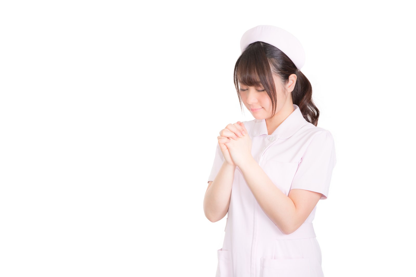ピンク色のナース服と白いナースキャップを着て、両手を合わせて祈る女性［モデル：茜さや］