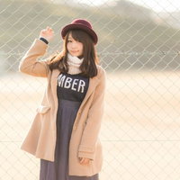 球場のフェンス前でコートを着た冬のカジュアルファッションの女性の写真