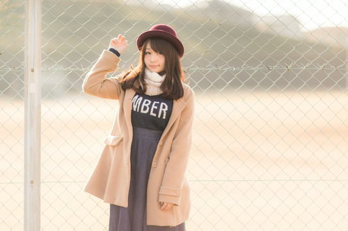 球場のフェンス前でコートを着た冬のカジュアルファッションの女性