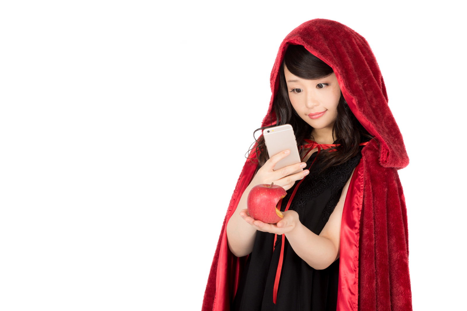赤いマントとフードを着た女性がスマートフォンを持ち、赤いリンゴを手にしている［モデル：茜さや］