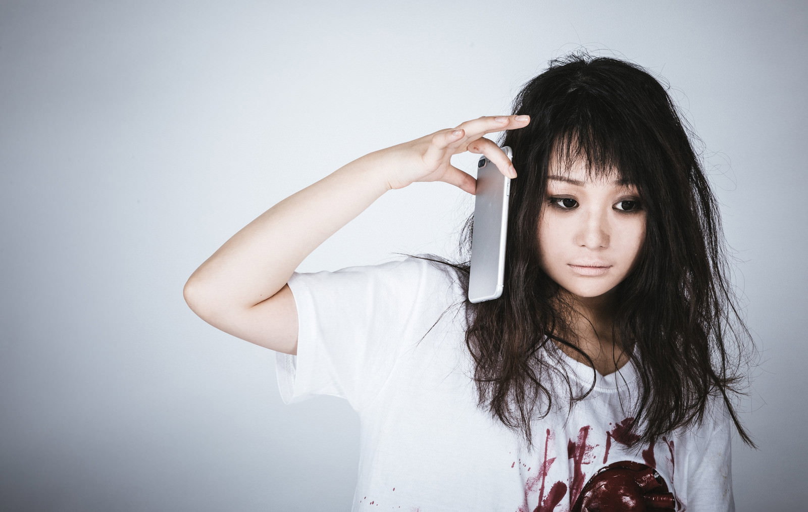 電話を耳に当てて通話している黒髪の女性［モデル：茜さや］