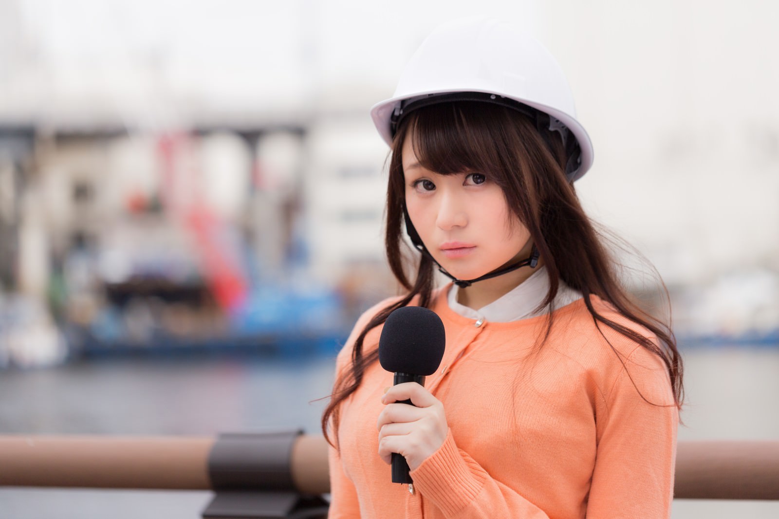 マイクを持つ女性アナウンサーが屋外で生中継している［モデル：茜さや］