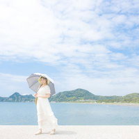 岩井海岸の防波堤で日傘を差す白いワンピースの女性と青空の写真