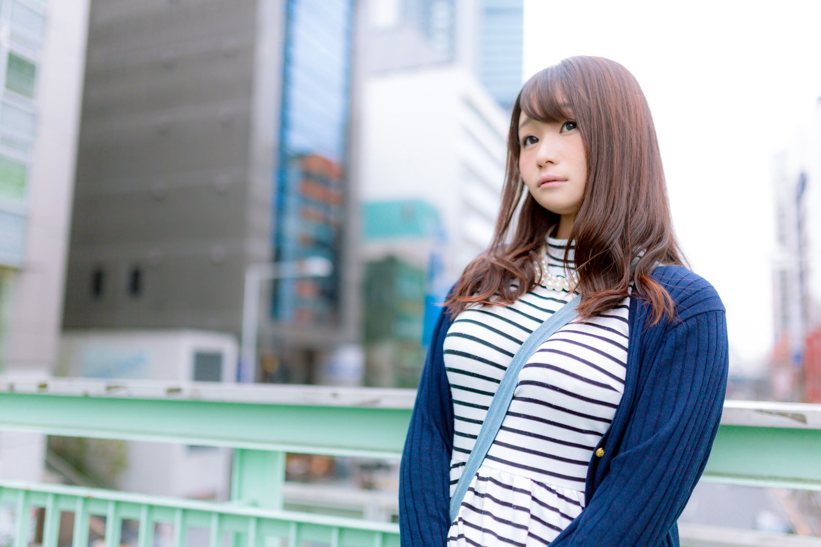 歩道橋で待ち合わせ相手を見つめる縞模様シャツの女性［モデル：茜さや］