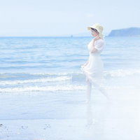 夏のビーチ、白いワンピース姿で波打ち際に立つ女性の写真