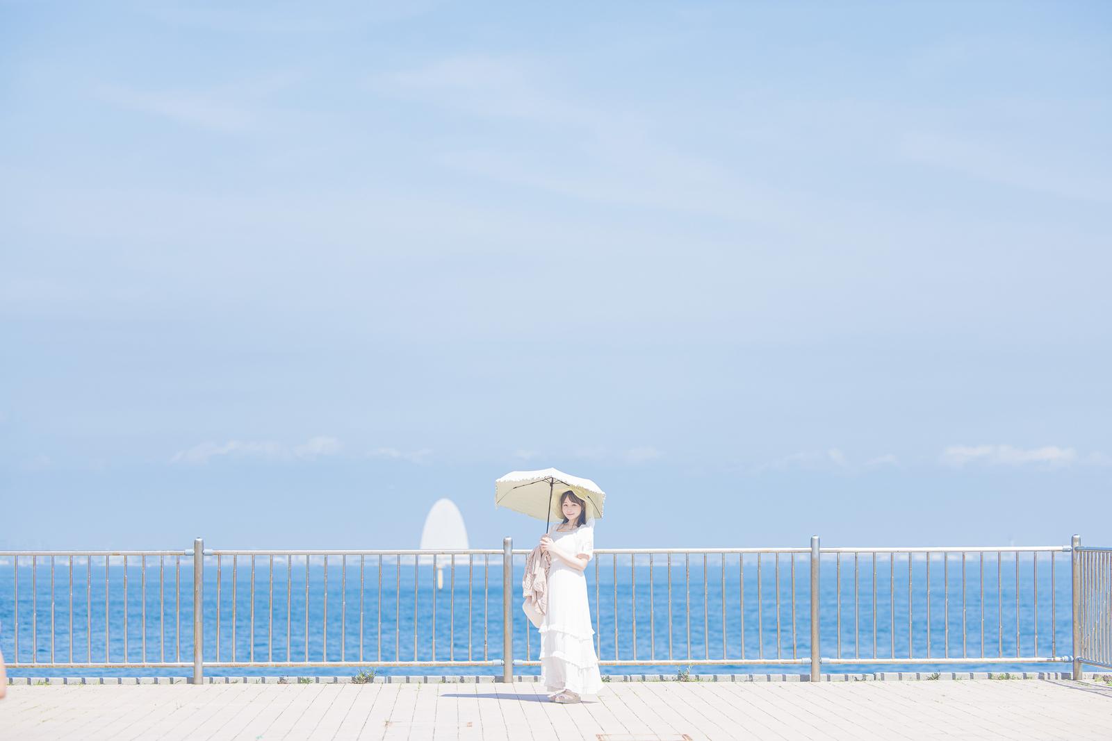 海ほたるの西展望デッキで日傘をさす白いワンピース姿の女性と青い海と空［モデル：茜さや］