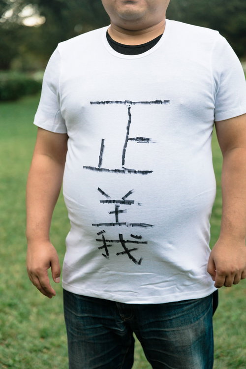 緑の芝生を背景に立つメタボ正義マン、白いTシャツに正義と縦書き