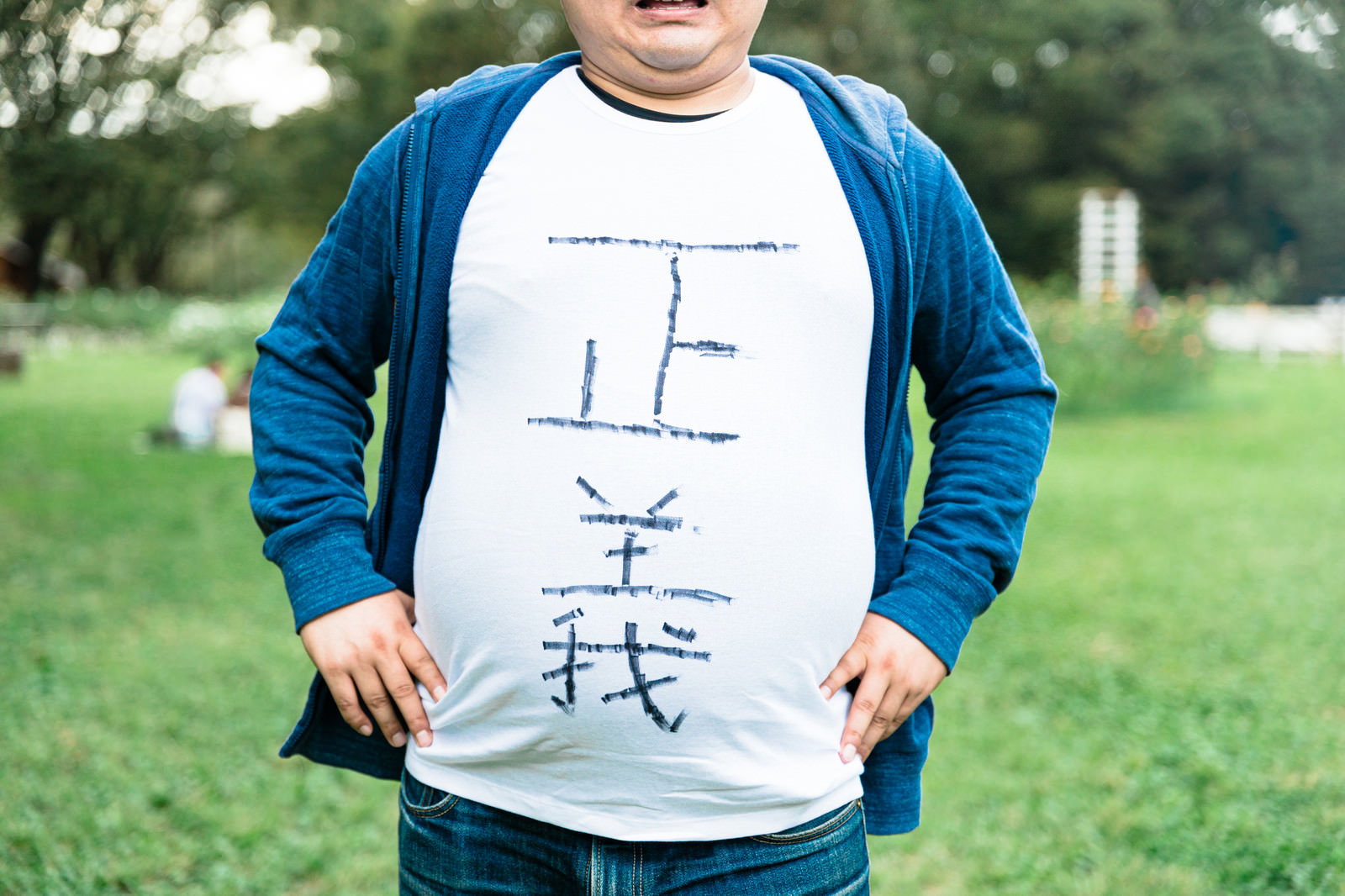 正義の文字が書かれた白いTシャツを着て公園の芝生の上に立つ男性［モデル：段田隼人］