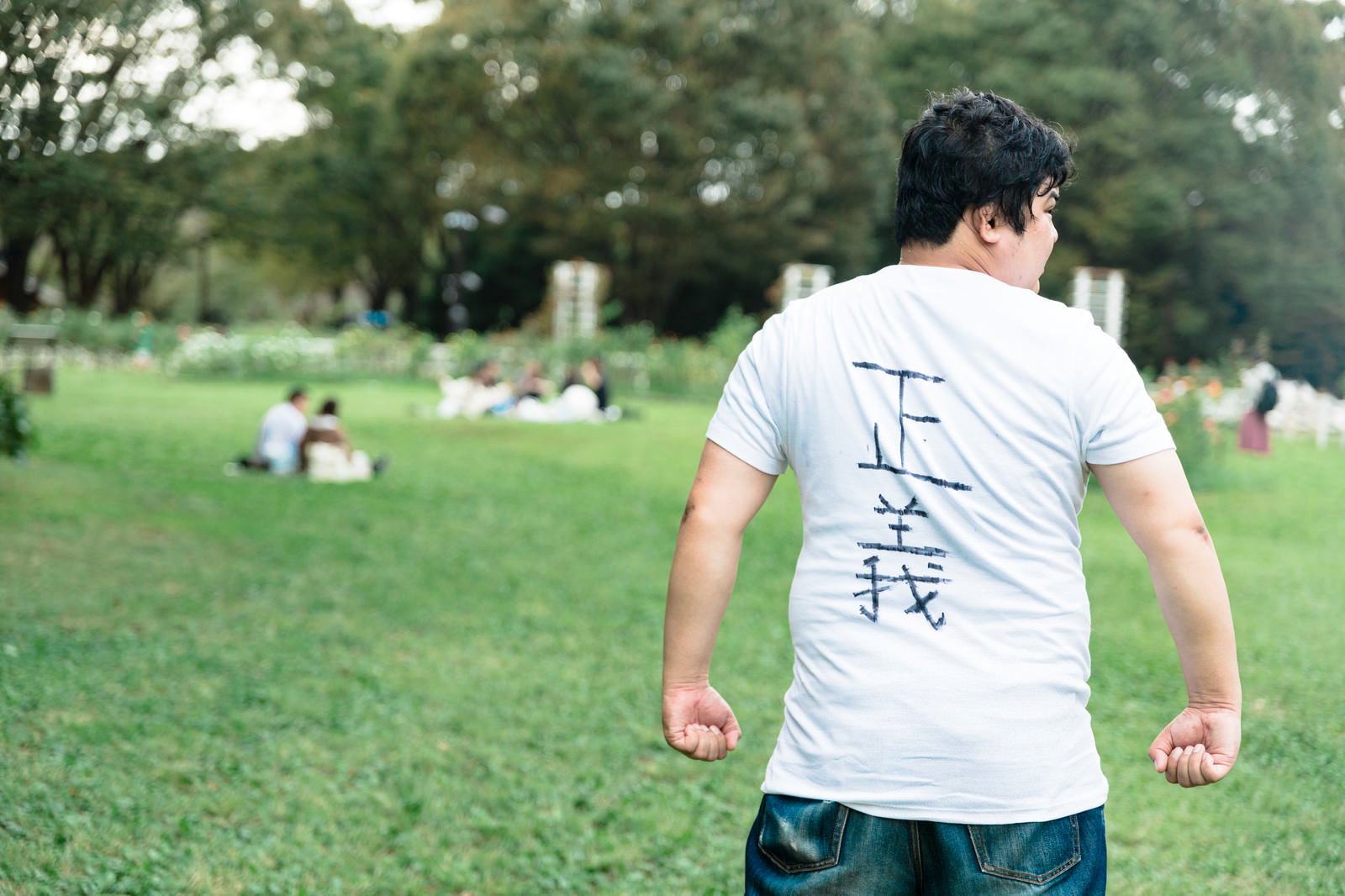 公園の芝生で後ろ姿を見せる白いTシャツの男性［モデル：段田隼人］