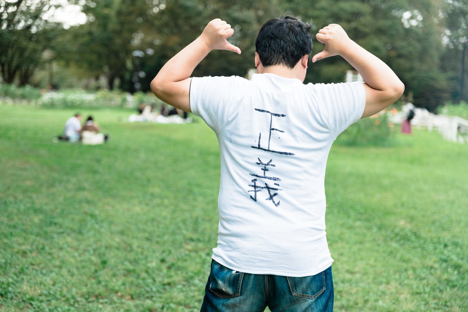 公園で背中の「正義」文字を見せながら力こぶポーズをする男性の後ろ姿［モデル：段田隼人］