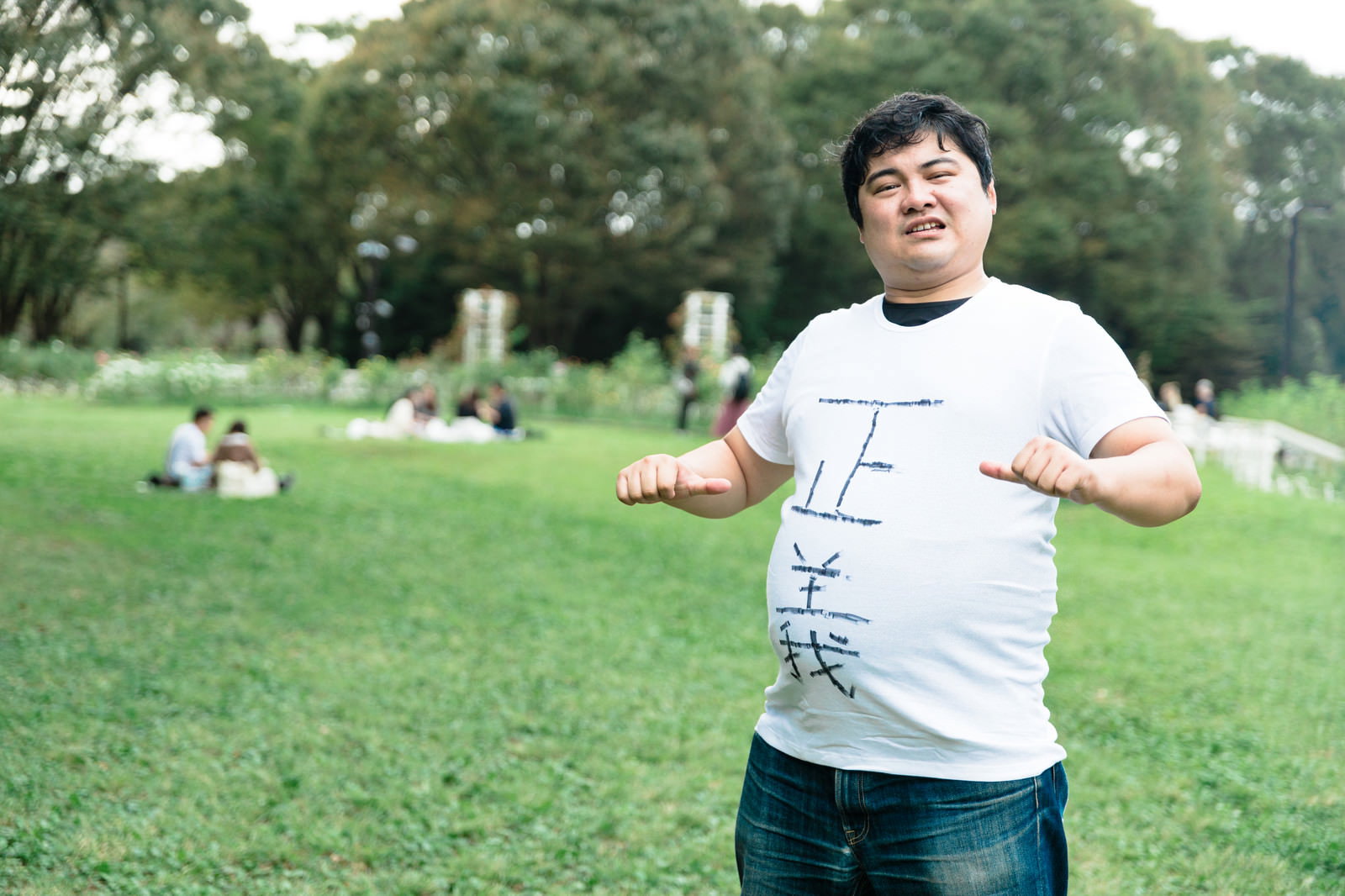 公園の芝生の上で白いTシャツを着た男性が両手を腰に当ててポーズを取っている［モデル：段田隼人］