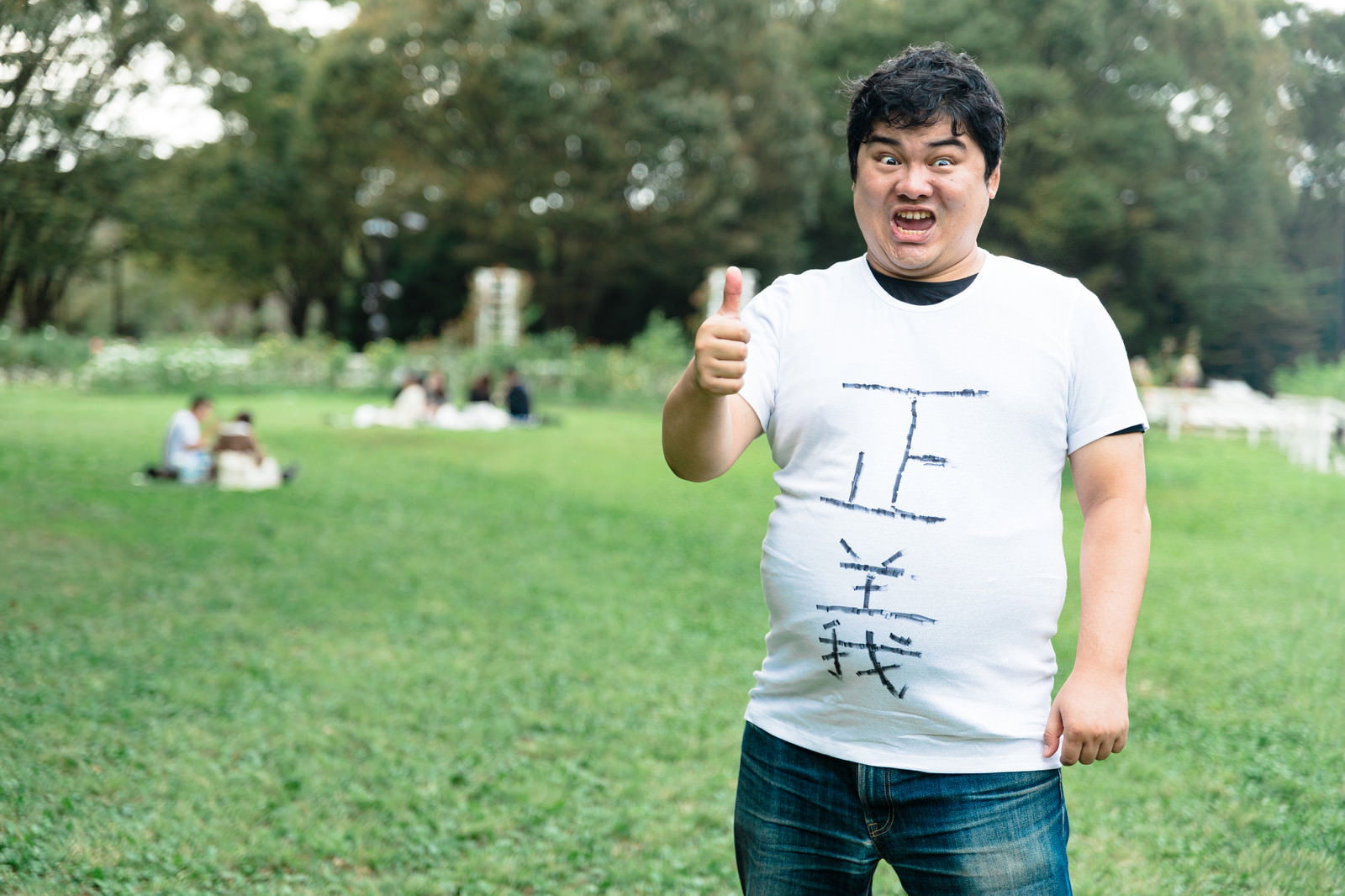 公園の芝生で白いTシャツを着た男性が親指を立てるポーズ［モデル：段田隼人］