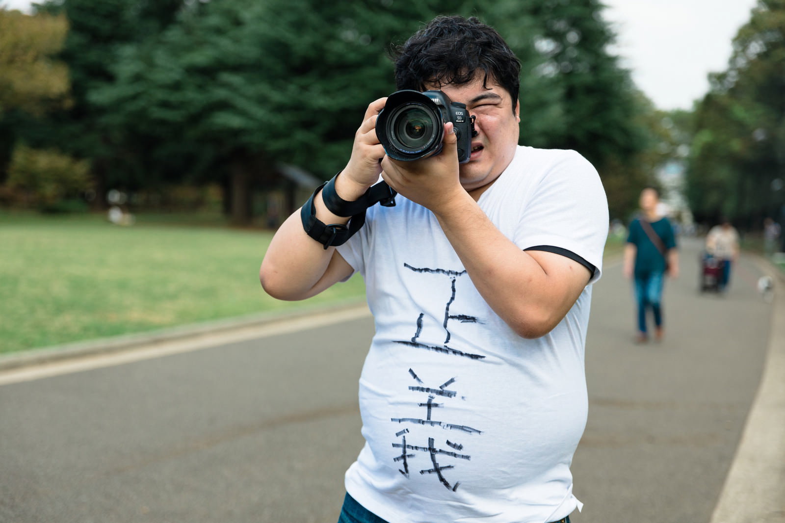 白いTシャツを着た男性が一眼レフカメラを構えて撮影している［モデル：段田隼人］