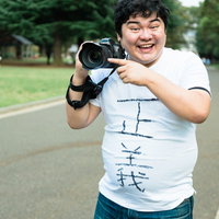 公園で一眼レフカメラを構えて笑う正義マンの写真