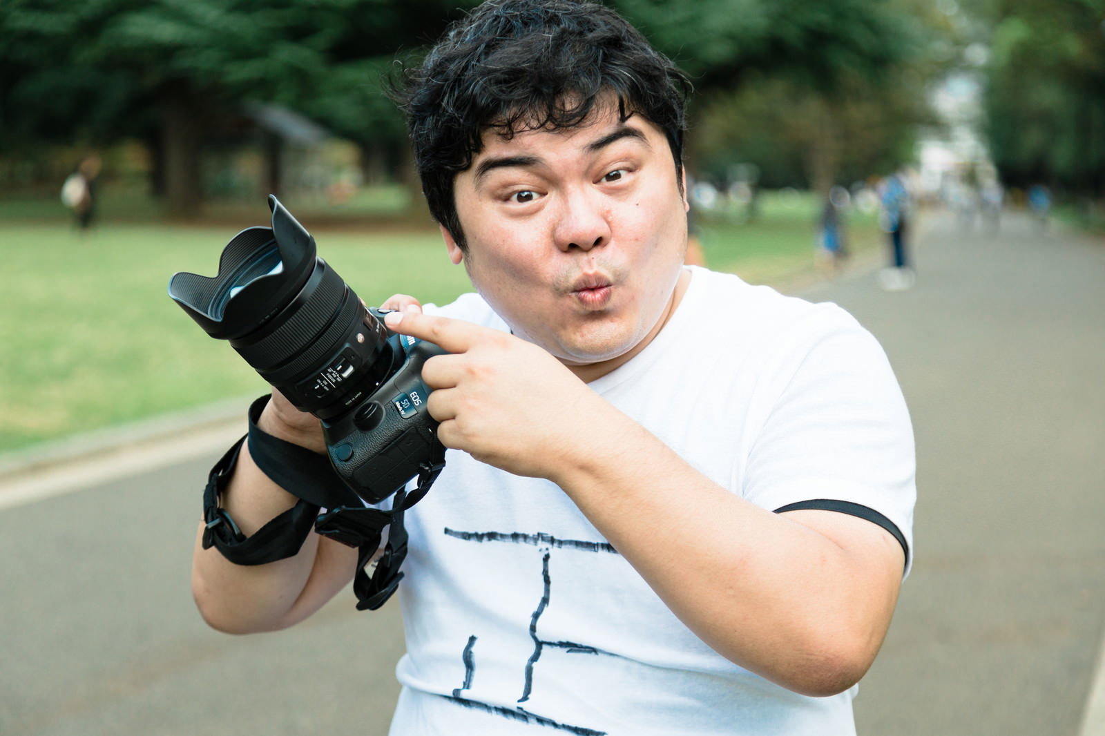 白いTシャツを着た男性が一眼レフカメラを構えている写真［モデル：段田隼人］