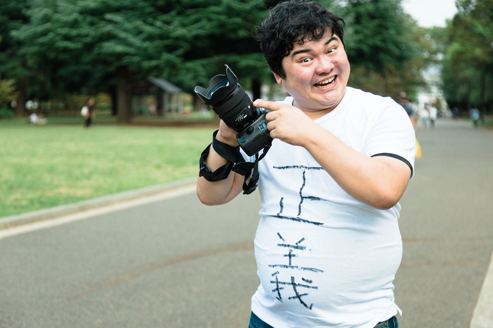 緑の公園で一眼レフカメラを抱えて笑顔を見せる男性