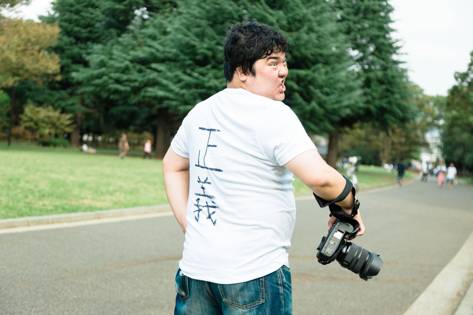 公園の路上でカメラを持った男性が振り返り、驚いて口を開けている姿［モデル：段田隼人］