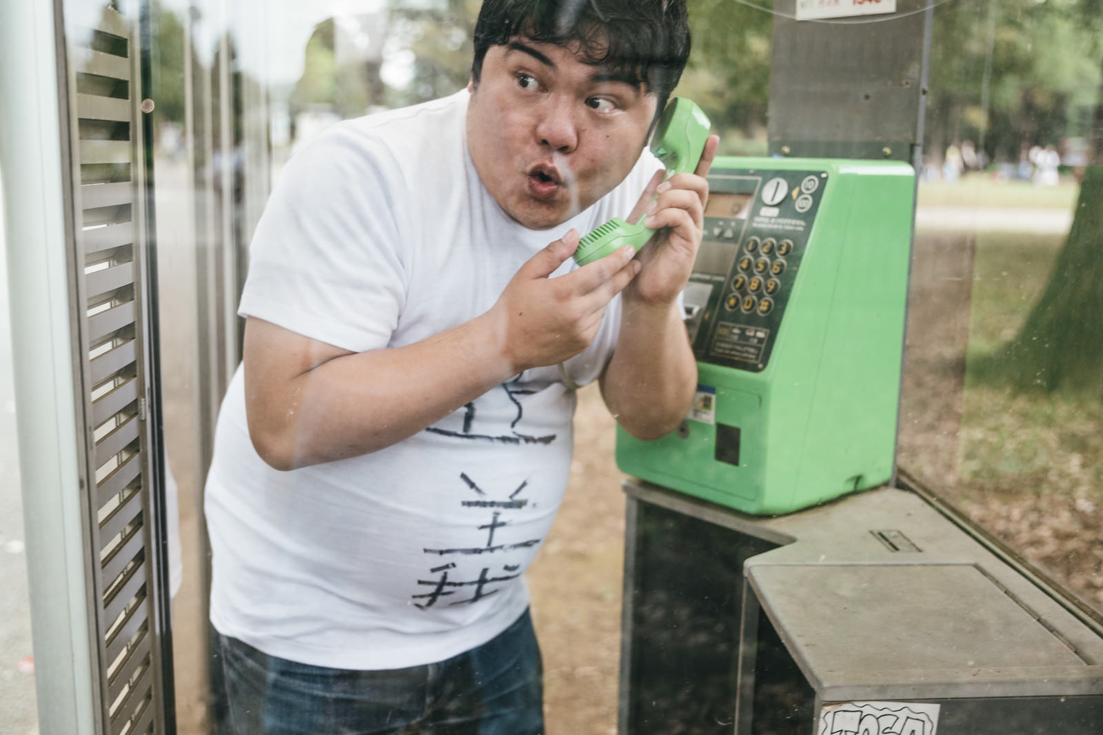 緑色の公衆電話で通報する白いTシャツの男性［モデル：段田隼人］