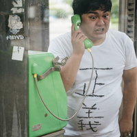 公衆電話から正義の通報をする白いTシャツの男性の写真