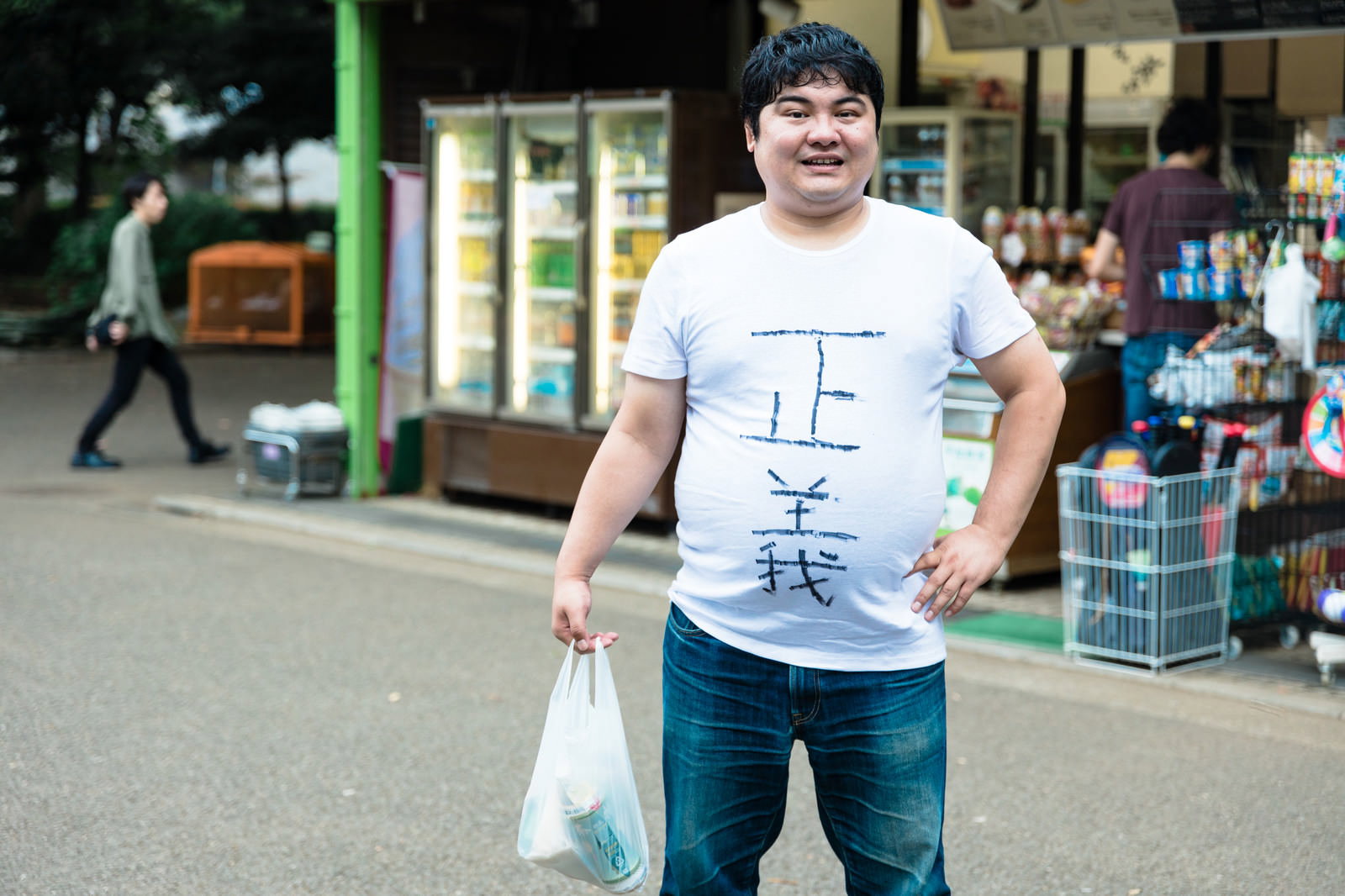 コンビニの前で紙を持った白いTシャツの男性［モデル：段田隼人］