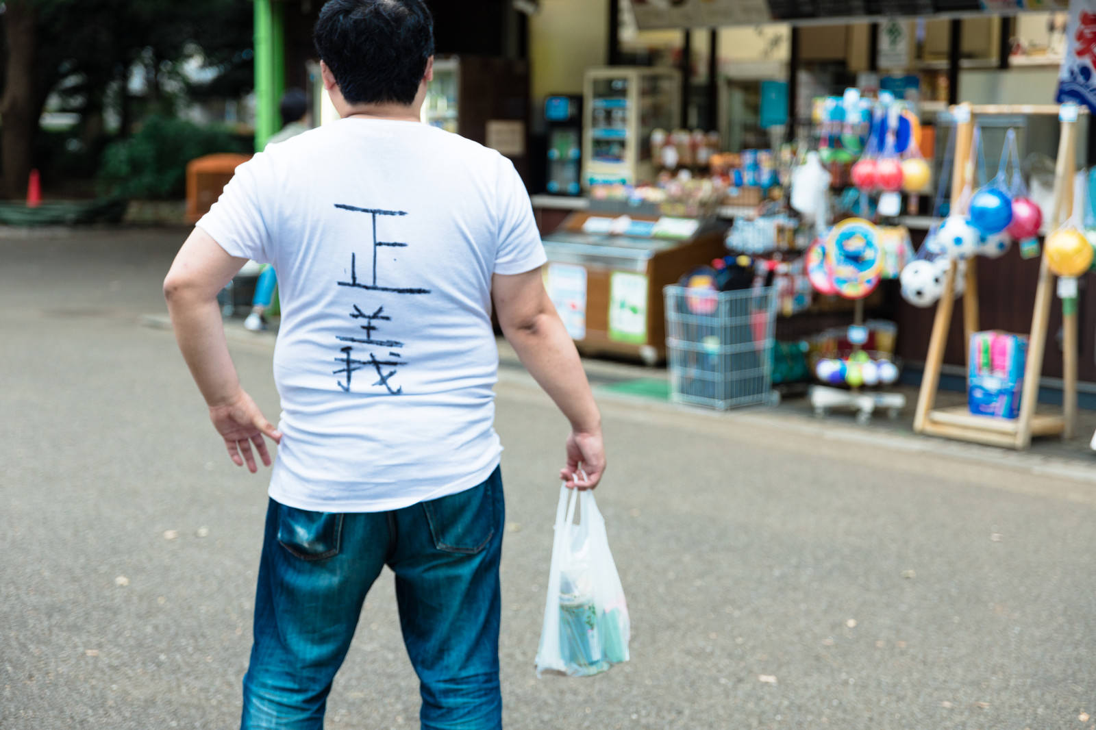 コンビニで買い物をする白いシャツの男性の後ろ姿［モデル：段田隼人］