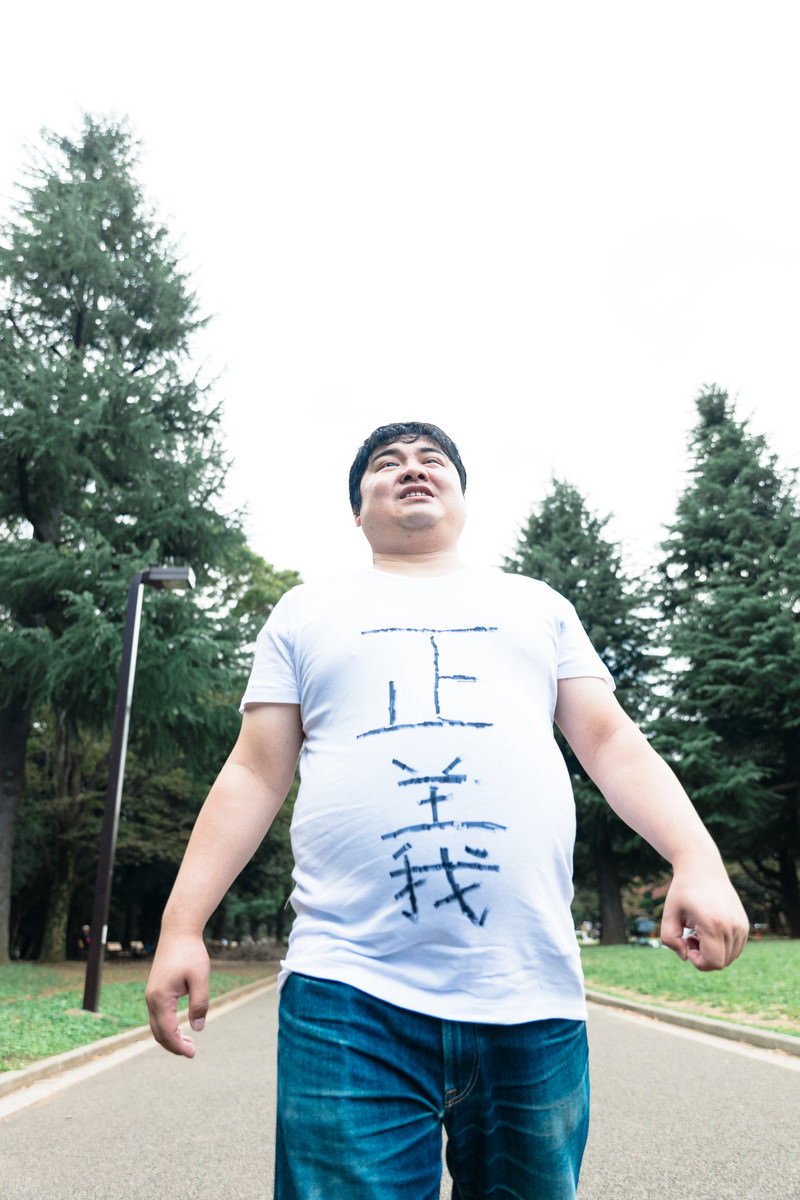 白いTシャツを着た男性が住宅街の道路で両手を広げて立っている［モデル：段田隼人］