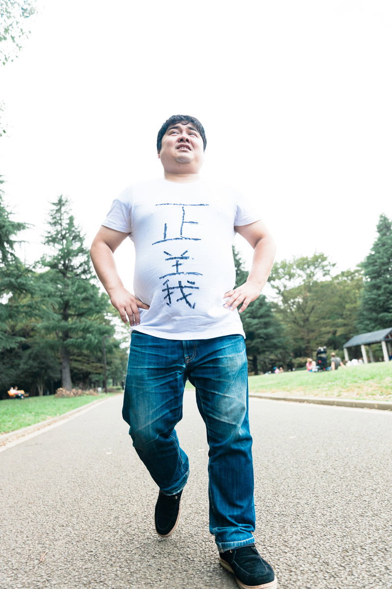 白いTシャツとジーンズ姿の男性が公園の道を歩いている様子［モデル：段田隼人］