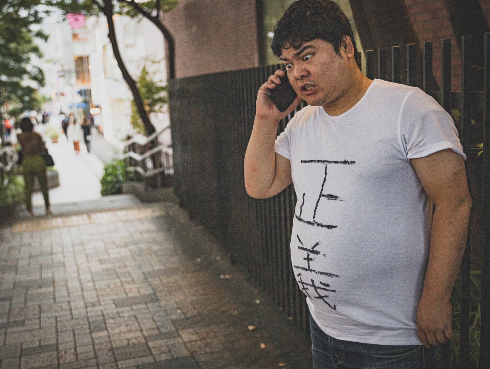 街角でスマートフォンで電話をかける白いTシャツの男性［モデル：段田隼人］