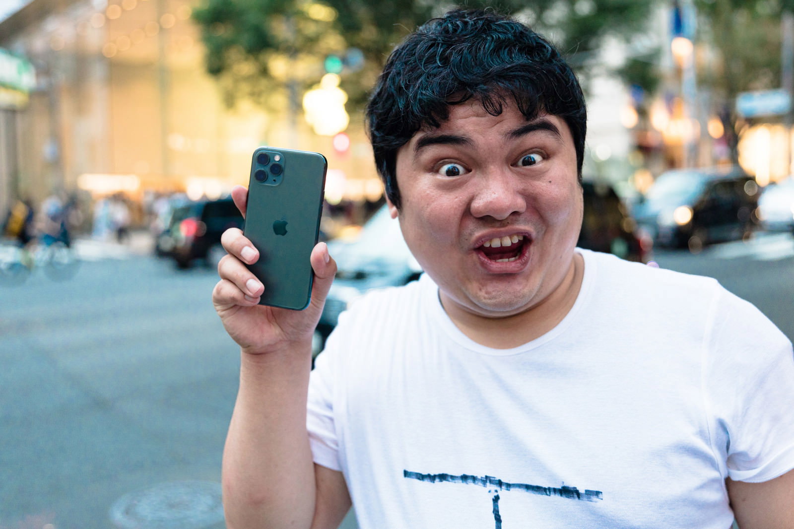 スマートフォンを持って驚いた表情を見せる白いTシャツの男性［モデル：段田隼人］
